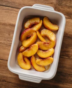 Halved peaches placed cut-side up in a white ceramic baking dish