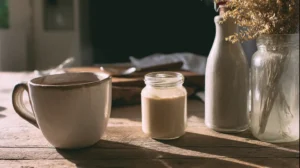 Low FODMAP coffee creamer in a glass jar next to a hot mug of coffee