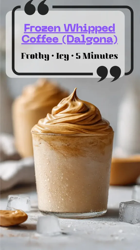 Side view tall glass of frozen whipped coffee—thick frappe base, glossy dalgona foam swirl, cocoa dust; straw and spoon; ice-cold, frothy coffee.