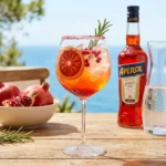 Aperol Spritz cocktail garnished with pomegranate seeds and orange slice.