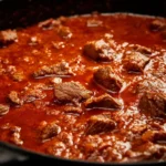 A delicious bowl of Nigerian beef stew garnished with fresh herbs.