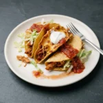 Plate of crispy mini baked chicken tacos with fresh toppings and salsa