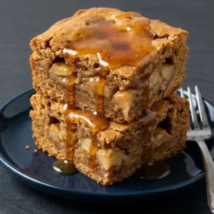Maple glazed apple blondies served on a plate with a drizzle of maple syrup.
